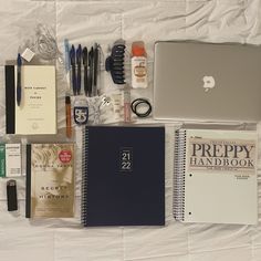 the contents of an apple laptop are laid out on a white sheet with pens, notebooks and other items