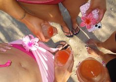 several women in bikinis are holding drinks and looking down at their butts on the beach