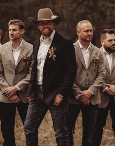 a group of men standing next to each other in front of trees wearing suits and hats