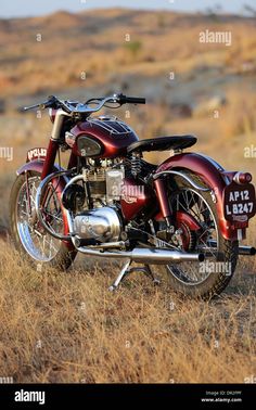 an old red motorcycle parked on the side of a dirt road in a dry grass field - stock image