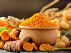 tumerical powder in a bowl surrounded by fresh tumerica and ginger roots