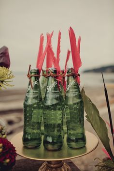 four green bottles are sitting on a table with red ribbons and flowers in the background