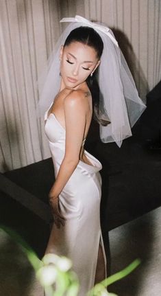 a woman in a wedding dress standing next to a bed with a veil on her head