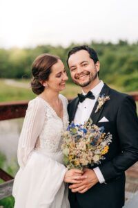 a bride and groom pose for a photo on a bridge in front of a river