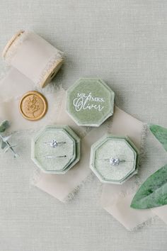 wedding rings and ring box on top of white cloth with green leaves next to them