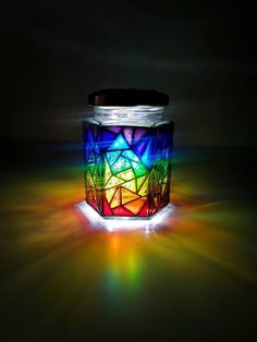 a colorful candle is lit up in the dark with light coming from it's top