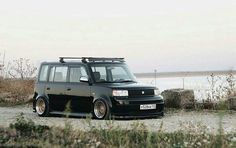 a black van parked on top of a gravel road next to the ocean and grass