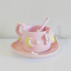 a pink cup and saucer sitting on top of a white table next to a spoon