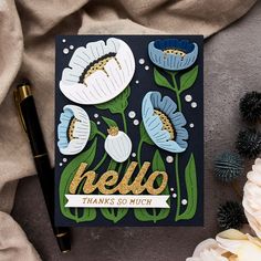 a card with flowers and the word hello on it, next to a pen and flower arrangement