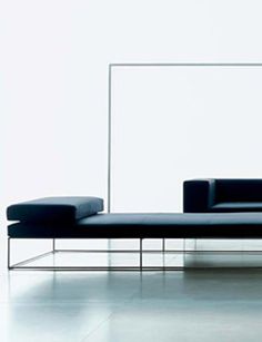 a black couch sitting on top of a white floor next to a glass wall with a mirror behind it