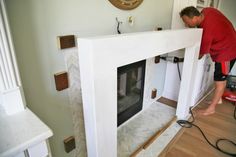 a man working on a fireplace in a living room with hardwood floors and white walls