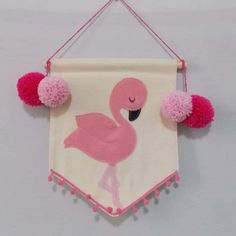 a pink flamingo hanging on a wall with pom - poms around it