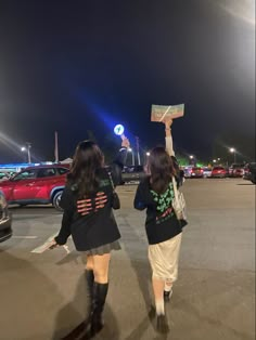 two women walking across a parking lot at night with their hands up in the air