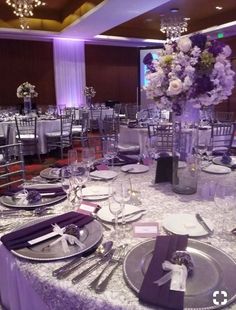 the table is set with silver plates and purple napkins