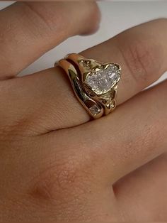 a woman's hand holding a gold ring with a heart shaped diamond on it