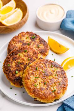 two crab cakes on a white plate with lemon wedges