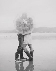 black and white photograph of two people hugging under an umbrella in the rain on a beach