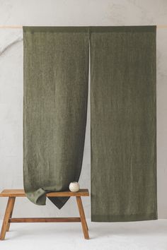 two green linen curtains hanging on a wooden stand with a white ball in between them