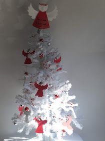 a white christmas tree decorated with red and white angel decorations, sitting on top of a table