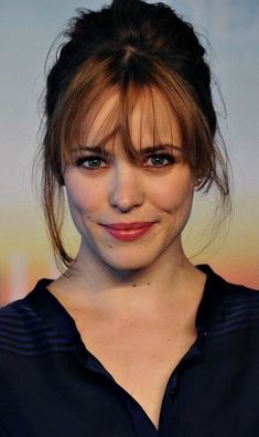 a close up of a person wearing a black shirt and smiling with her hair in a bun