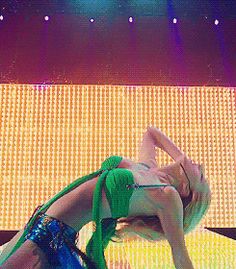 a woman in green and blue is performing on stage with her legs spread out to the side