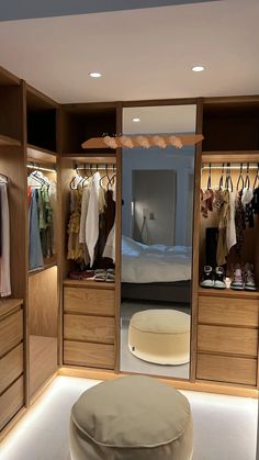 a walk in closet filled with lots of clothes and shoes next to a round ottoman