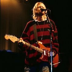 a man standing in front of a microphone while holding a guitar