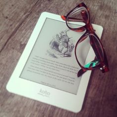 a tablet with glasses on top of it sitting on a wooden table next to a pair of reading glasses