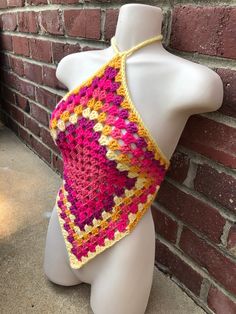 a white mannequin wearing a pink and yellow crocheted shawl against a brick wall