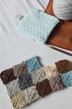 two crocheted squares sit on a table next to a ball of yarn and a book