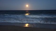 the moon is setting over the ocean with waves