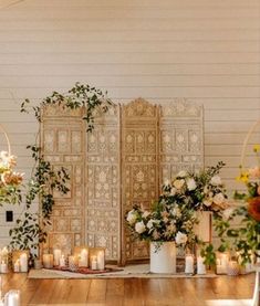 an arrangement of flowers and candles on a wooden table in front of a white wall