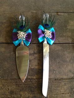 two spoons with purple and blue ribbons on them are next to each other, one has a peacock tail