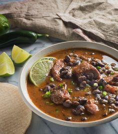 a white bowl filled with black beans and limes next to some sliced jalapenos