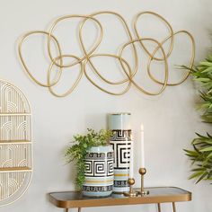 a table with two vases on it next to a wall sculpture and potted plant