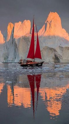 a sailboat with red sails in front of icebergs