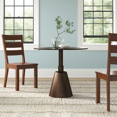 a small table with two chairs and a vase on the top, in front of three windows