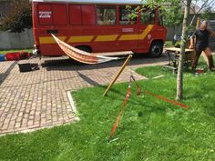 a red bus parked next to a tree with a hammock hanging from it