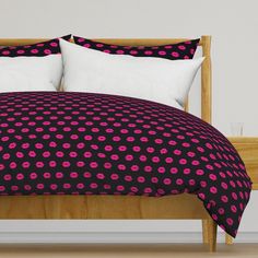 a bed with black and pink polka dot comforter set on top of wooden headboard