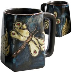 two coffee mugs with dragonflies painted on the inside one is black and gold