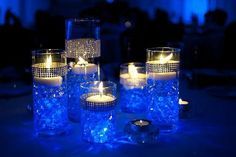 several lit candles are sitting in glass containers on a table with blue lights around them