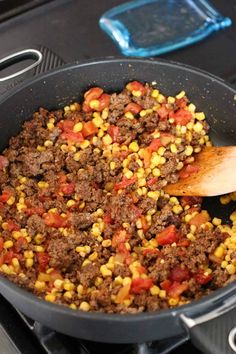 corn and ground beef cooking in a skillet with a wooden spoon on the stove