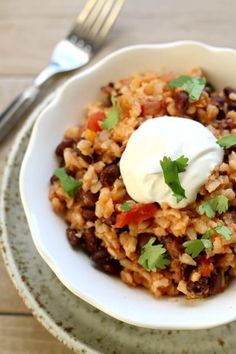 a bowl filled with rice, beans and sour cream on top of a wooden table