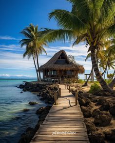 a wooden dock leading to a hut on the water with palm trees in the foreground