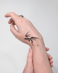 a hand with a small dragon tattoo on it's left wrist and the other hand is holding another one