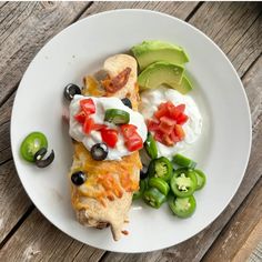 a white plate topped with an enchilada covered in sour cream and toppings