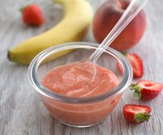 a small glass bowl filled with strawberry and banana dip next to some fruit on the table