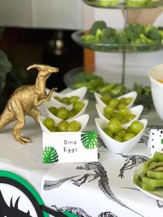 a table topped with bowls filled with grapes and veggies covered in gold dinosaur figurines