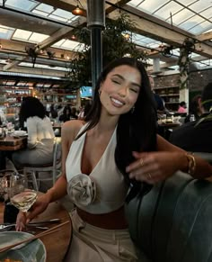 a woman sitting at a table with a glass of wine in her hand and smiling