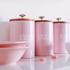 three pink kitchen canisters sitting on top of a counter next to a bowl